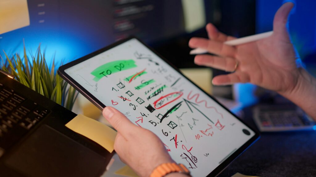 Two hands holding tablet and stylus with messy to-do list on the screen