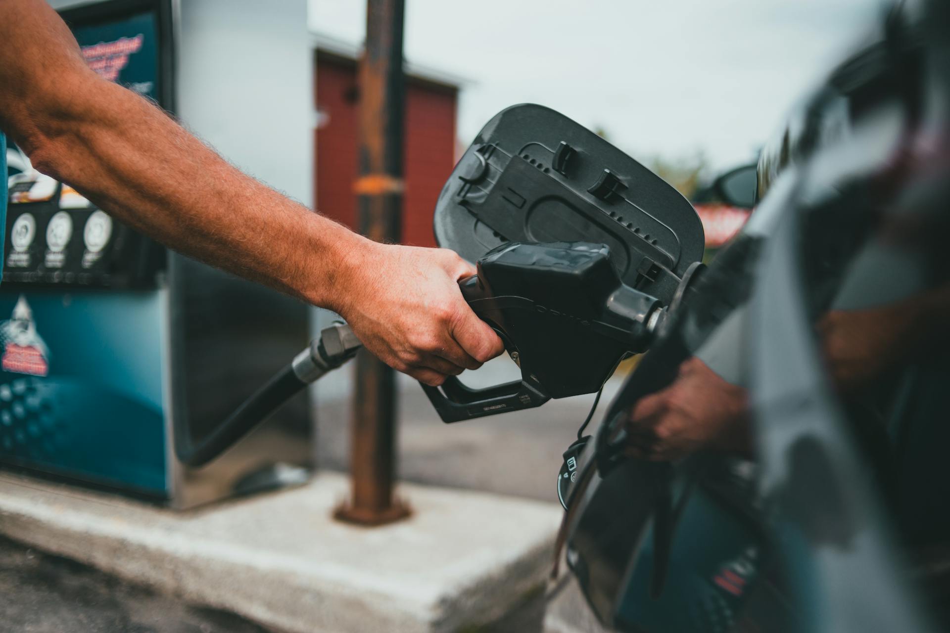 Hand holding petrol nozzle putting fuel into car